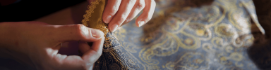 Woman sewing on fabric, working on tailoring with focused attention and sewing tools nearby.
